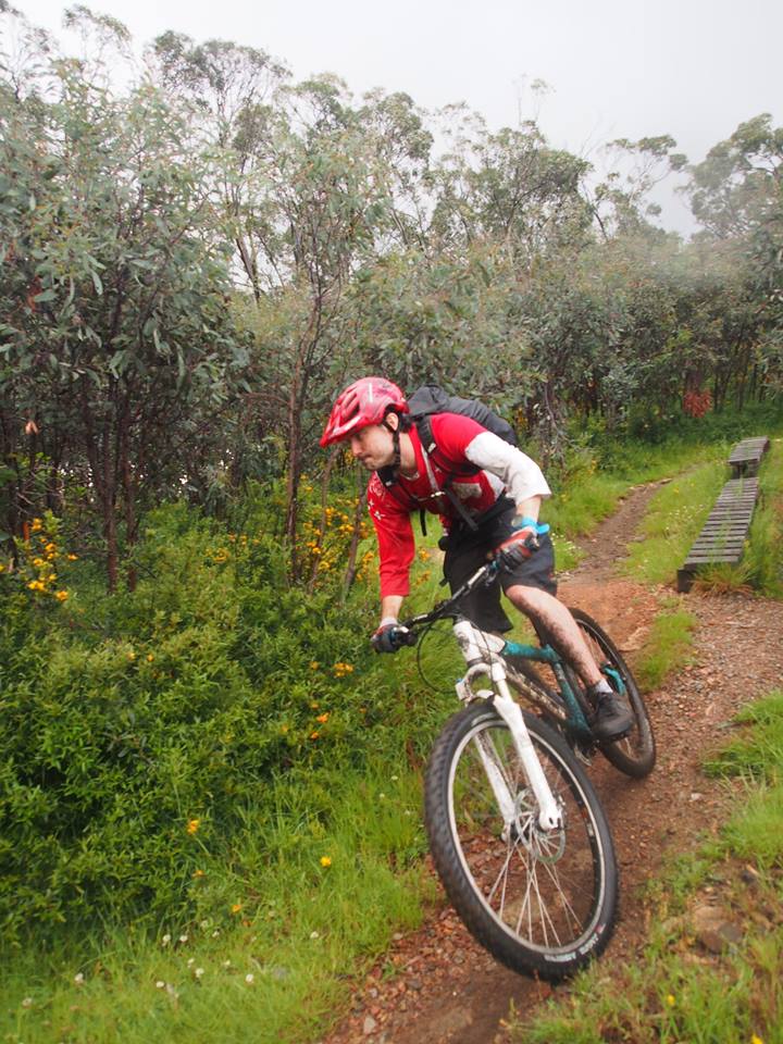 A male mountain biker in a red shirt riding down hill and turning.